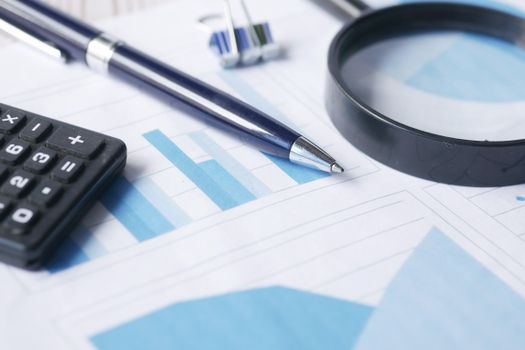 Calculator, pen and magnifying glass on financial charts